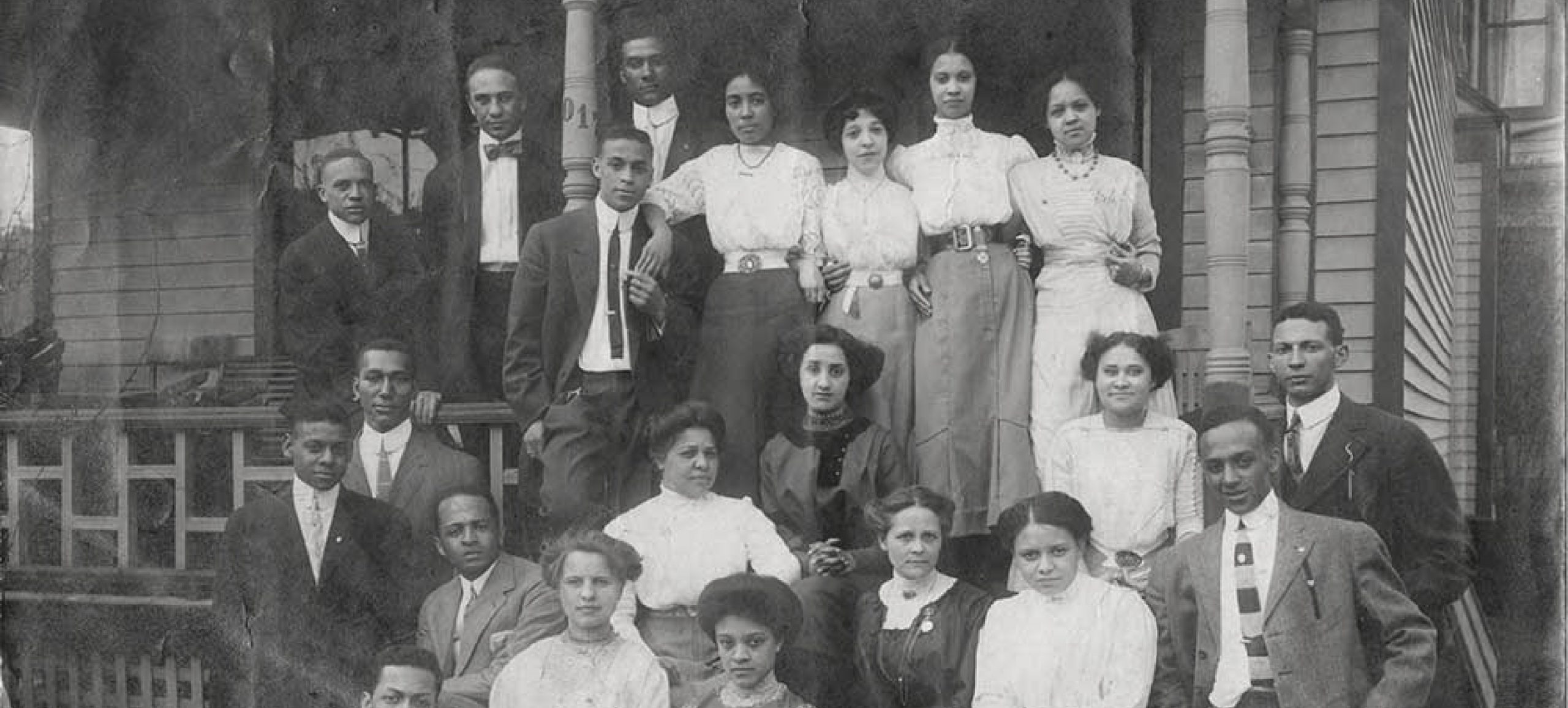 A group of male and female African American students on the front steps and porch of the Alpha Phi Alpha fraternity house in Ann Arbor. ca.1912.